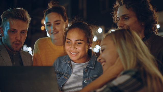 Beautiful and Handsome Friends are Using a Laptop Computer while Standing at a Table in an Outdoors Street Food Cafe. They're Watching a Video or an Online Stream. They are Happy and Smile.