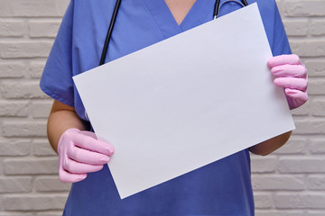 Doctor holds an empty blank sheet of paper, copy space for the inscription. Woman nurse in a blue uniform with a white sheet, close-up