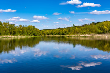 Naklejka na ściany i meble landscape of a beautiful wide river on a sunny day with blue reflection with beautiful clouds in the water