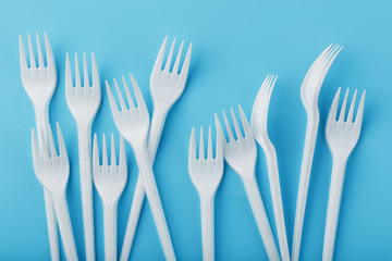 White plastic forks of disposable tableware on a blue background.