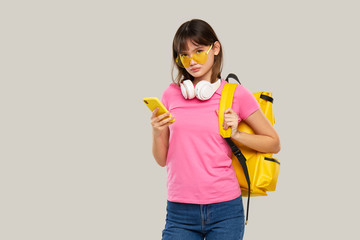 An Asian teenager girl in heart-shaped glasses holds a mobile phone in hands  on gray background. New Gadget Advertising