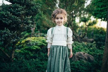 girl in a green-white dress stands by a tree