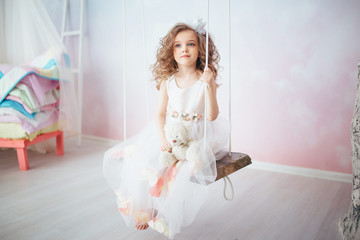 little girl in a white dress sits on a wooden swing