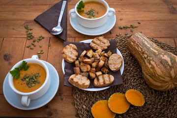 Top view of wooden rustic table and pumpkin cream in two white bowls, bread croutons and seeds