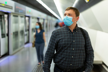 Fototapeta na wymiar Male in protective medical mask is traveling and waiting train on platform in the metro.