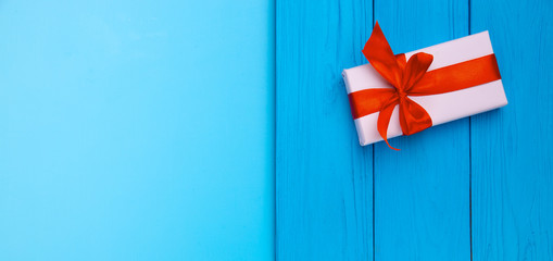 Box in Kraft paper, ECO-paper on a wooden table. View from the top. A white paper-wrapped gift box with a red satin ribbon bow on an old rustic blue wood background. Copying space for text.