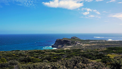 The legendary Cape of Good Hope in South Africa. Unusual rocky cape protrudes into the Atlantic Ocean. The waves beat against the rocks and foam. The cape is covered with green plants. 