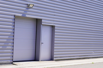 Obraz na płótnie Canvas grey metal roll-down shutters on vertical profiled sheeting gray building fire exit door in commercial industrial unit