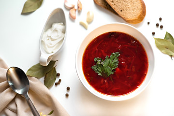 Beetroot soup in white bowl on a white table served with napkin, garlic, pepper, bread and saucy with sour cream. Traditional ukrainian, russian soup borscht with greens. Top view.