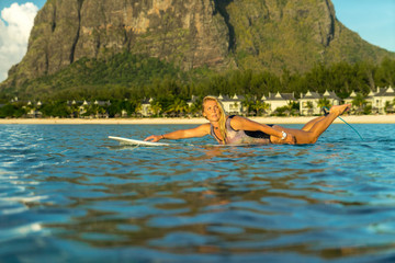 A beautiful girl rowing on a surfboard in the ocean against the backdrop of a picturesque mountain