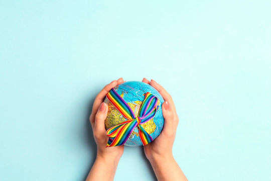 Female hands holding globe with LGBT rainbow ribbon on blue background. LGBT community.