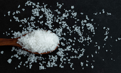 Top view flower of salt in wooden spoon on dark background. Selected focus.  Free copy space on right.
