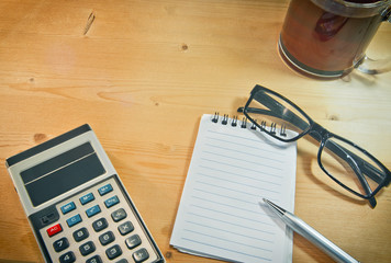 an old calculator black glasses a notepad a pencil and a cup of coffee on a yellow wooden board