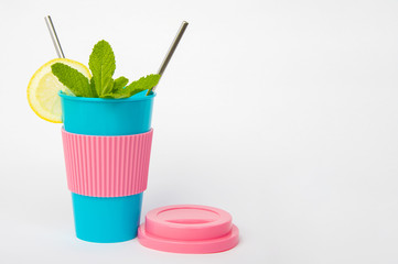 Reusable blue cup with pink silicone sleeve and lid, with metal straws, lemon and mint. Healthy lifestyle concept and Eco friendly concept