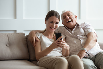 Overjoyed mature 80s father and adult daughter sit rest on couch in living room laugh watching...