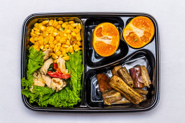 Healthy diet meal plan with corn, shredded chicken, veggies and oranges in bento box top view