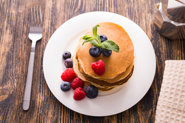 Homemade sweet pancakes with blueberries and raspberries on a white plate, top view.