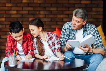 Smiling scholar girl sitting with brother and writing on textbook. Happy child doing homework at elementary school.