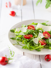bright and healthy salad with arugula, cocktail cherry tomatoes, parmesan on a white wooden table