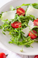 bright and healthy salad with arugula, cocktail cherry tomatoes, parmesan on a white wooden table