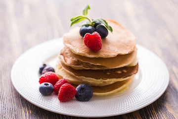 Pile of pancakes with blueberries and raspberries for breakfast on wooden table.