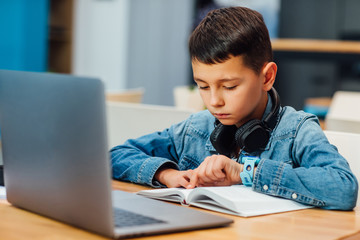 Portrait of concentrated boy with laptop doing homework and writing.