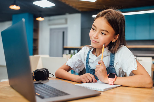 Pretty girl using a laptop computer for homework at modern blue classroom.
