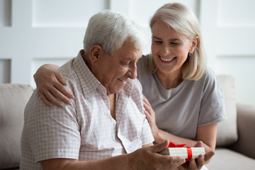 Smiling mature wife hug excited senior 80s husband greeting with birthday or anniversary with gift...
