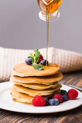 Maple syrup pouring over a stack of mini pancakes.