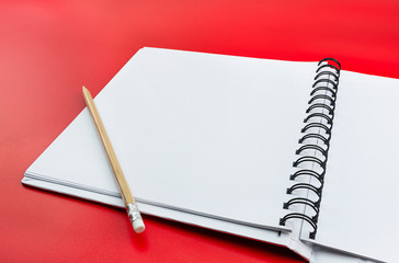 An open notebook with white pages and a wooden pencil lying on the left, isolated on a red background.