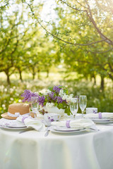 Holiday decorated dining table in the spring garden.  Lilac flowers in vases on the table. Purple style. French Provence
