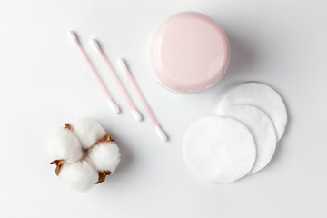 Cosmetics and self-care. On a white background, cotton pads, cotton sticks, a cotton flower and a jar of cream are beautifully laid out. Flat lay