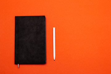 black notebook and pen on white background orange paper, the concept of minimalism.