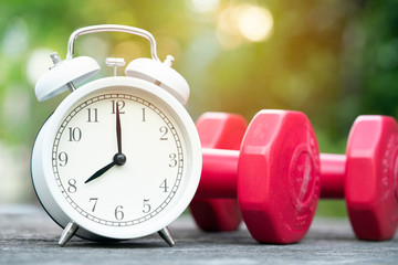Time for exercising alarm clock and dumbbell on the table background