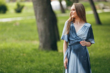 Fototapeta premium Stylish girl posing in a dress in a sunny spring park. Cheerful, happy portrait of a beautiful girl in the summer