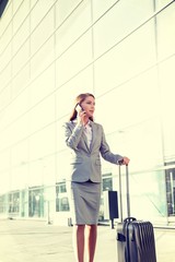 Portrait of young attractive businesswoman talking on smartphone with her suitcase in airport