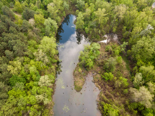 Fototapeta na wymiar A small lake in a deciduous forest. Clouds are reflected in the water. Aerial drone view.