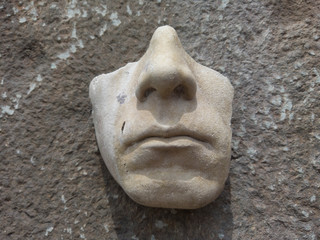 Close up of partial face in stone against an old brick, sandstone and cement wall 