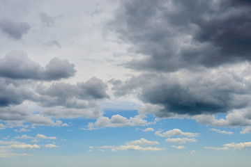 Dark thunderclouds are approaching the blue sky with white clouds. Change of weather from sunny to rainy. Dramatic skyscape.