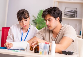 Fototapeta premium Young man with bandaged arm visiting female doctor traumatologis