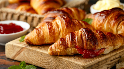 Freshly baked croissants with butter, strawberry jam and tea for breakfast or brunch