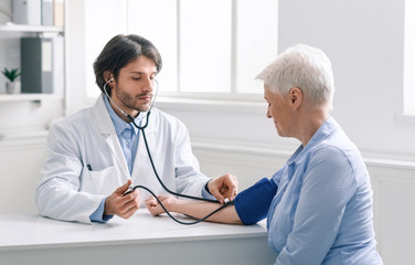 Young doctor measuring blood pressure of senior woman