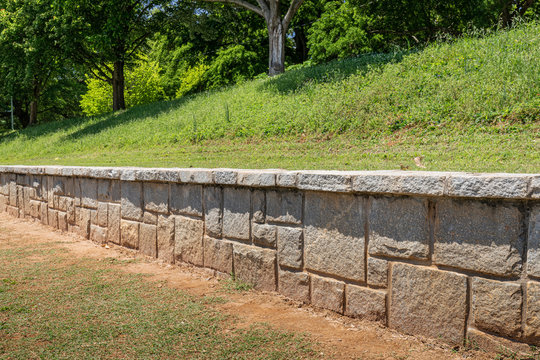 Stone retaining wall in a public park, green hills with ground cover and trees, horizontal aspect