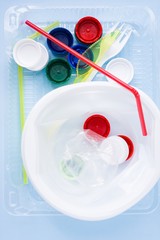 Pile of single use plastic garbage including water bottles, drinking straws, plate, fork, knief and bottle caps in box for food