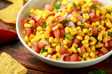 Mexican Corn Salsa in white bowl with lime and tortilla chips on wooden table. Healthy food