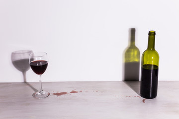 Bottle with wine and glass, red puddle of wine on the table. Cleaning after party concept.