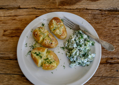 Baked potatoes with cheese and cocumber salad with sour cream on white plate.