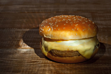 Cheeseburger with egg on a pink wooden background. Burger with contrasting dramatic light. A table made of old shabby boards.