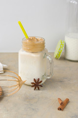 Iced Dalgona Coffee, a trendy fluffy creamy whipped coffee. Glass mug, bottle of milk, spices on a light background. Whisk from a blender on a stand. Vertical position.