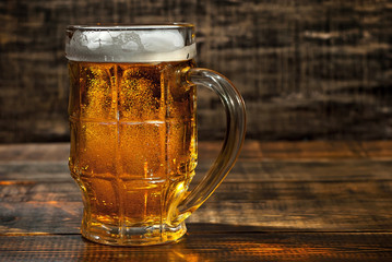 A glass of amber beer. Glasses on a wooden table. Black shabby boards on the background. Bright...
